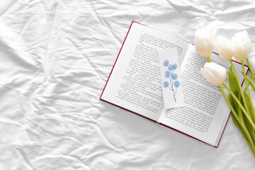 Book and beautiful flowers on bed