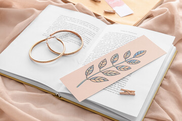 Book with bookmark and earrings on color background