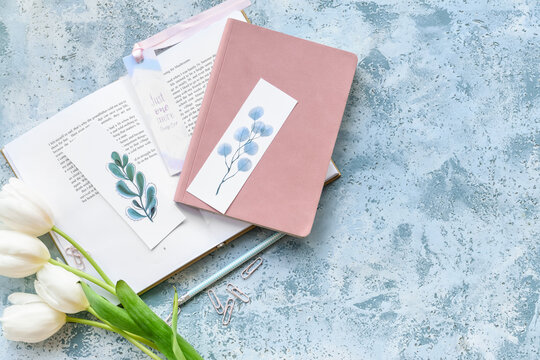 Book with bookmarks, notebook and flowers on color background
