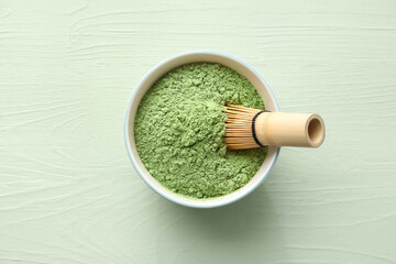 Bowl with powdered matcha tea and chasen on color wooden background