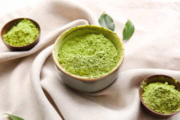 Bowls with powdered matcha tea on light fabric background, closeup