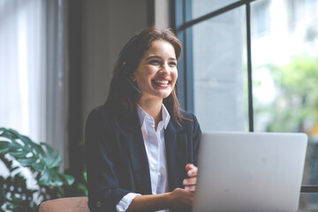 Attractive business woman Asian in suits and headsets are smiling while working with computer at office. Customer service assistant working in office. VOIP Helpdesk headset