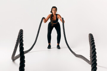 Sporty young woman in black suit doing crossfit exercises with ropes over isolated white...