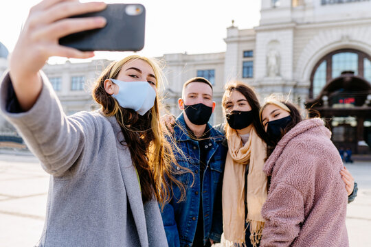 Happy millennials friends taking a selfie and wearing protective face masks. Concept of health care and the new normality.Focus on the woman on the left.