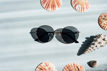 Obraz premium Sunglasses on a blue background with shells. direct sunlight and shade. Space for the text.