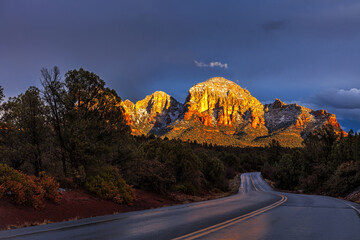 Sedona at nightfall.  A winding road leads to red rocks illuminated by the setting sun
