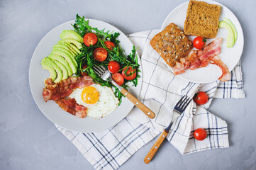 tasty homemade breakfast - fried eggs with bacon served with toasted bread, arugula tomato salad and fresh avocado