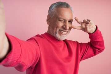 Positive man shows V sign, gesture of victory, peace, making selfie. Handsome, smiling man posing on pink background, copy space, place for text.