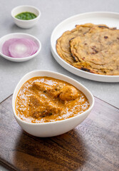 butter chicken, an Indian creamy chicken gravy served in a white bowl with roti or naan