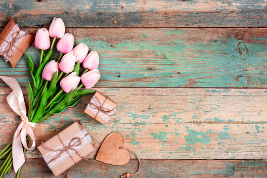 Bouquet of pink tulips with gifts and heart on shabby wooden turquoise boards.