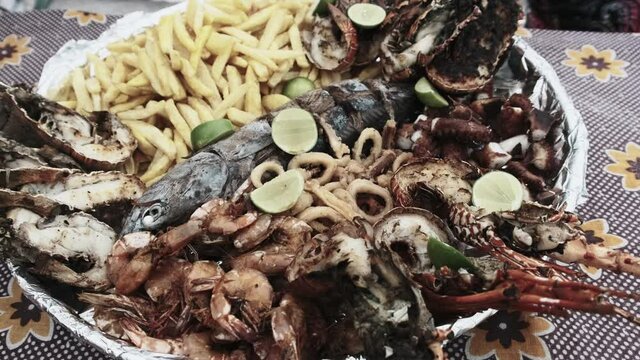 Plate with seafood. Large platter of deliciously cooked squid, shrimp, crab, lobster, octopus and tuna is served on a table near beach. An exotic lunch for tourists in Africa. African style. Zanzibar