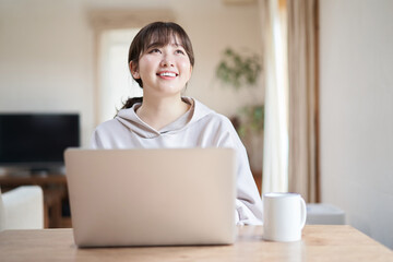 リビングで笑顔でパソコン操作をするアジア人女性