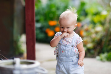 Naklejka premium funny emotional toddler baby in the summer in the village, iron large can and garden paths. The first steps