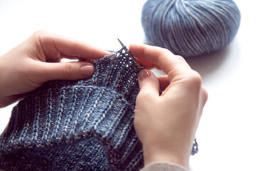 Female hands with knitting needles to knit wool violet sweater and tangle of woolen thread on white background. Woman knitting woolen clothes. Overhead shot. Handicraft earnings concept