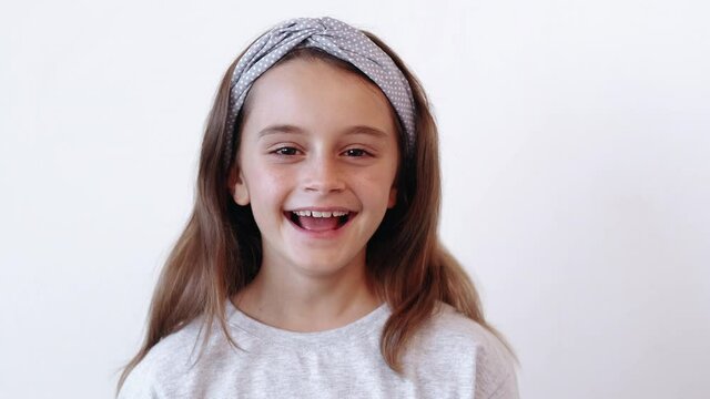 Amazed child. Awesome surprise. Unexpected news. Happy excited impressed little girl covering open mouth with hands showing wow reaction isolated on light neutral empty space background.