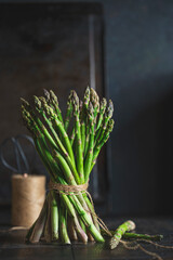 Fresh stems of green asparagus with spices around - salt crystals , dark wooden background. Macro view, copy space. Vegan, healthy eating, dieting concept. Organic vegetables.