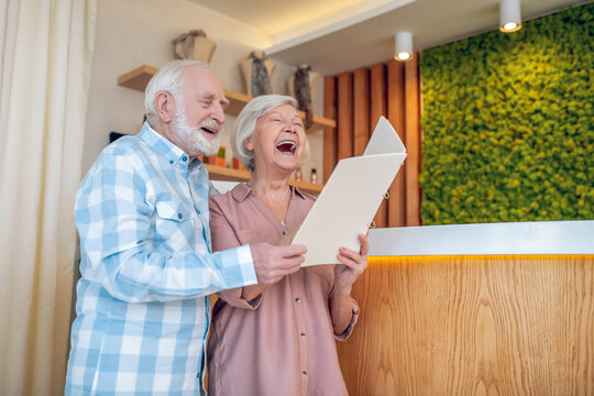 Gray-haired couple standing near reception in a spa center and laughing