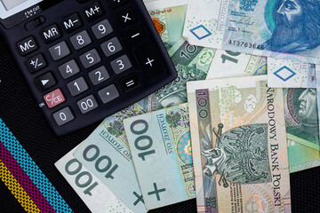 Calculator and Polish banknotes of PLN 100 and PLN 50 on a black background. Photo taken under soft artificial light