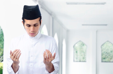 Asian Muslim man standing while raised hands and praying