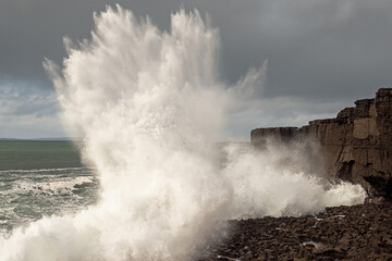 Power full ocean wave breaks on rock shore line creating big splash of water. Storm on West coast...