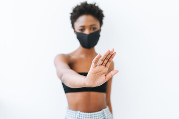 Beautiful young African American woman in black top and face mask isolated on white background, stop coronavirus concept