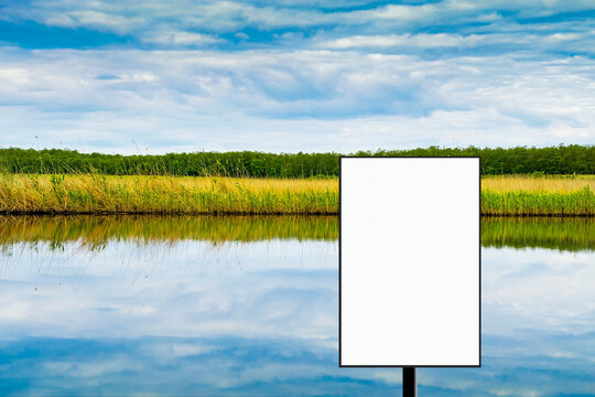 Blank vertical billboard against the backdrop of the river and the cloudy sky. Mockup. Copy space.