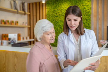 Young dark-haired cosmetologist showing the list of procedures to a customer
