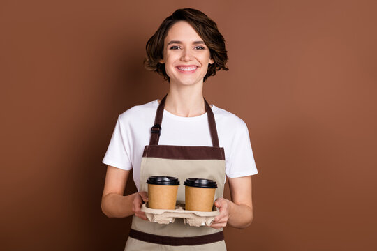 Portrait of attractive cheerful girl carrying bringing caffeine latte cappuccino isolated over brown color background