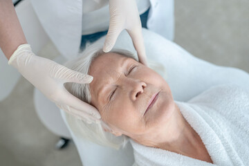 Fototapeta na wymiar Gray-haired mature woman having a face massage and looking relaxed