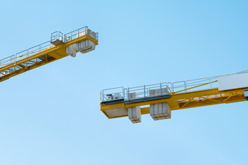 Two arms of yellow construction cranes with concrete weights face each other.