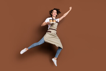 Fototapeta na wymiar Full body portrait of excited cheerful lady hold coffee cups raise fist up flying isolated on brown color background