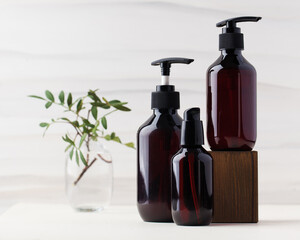 Three different brown glass bottles with natural organic cosmetics products on wooden block with...