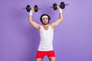 Photo of guy raise hands hold heavy dumbbells make effort wear sportswear spectacles isolated violet background