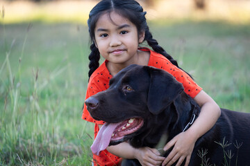 A young girl in red outfits plays with her big black dog in the backyard in the evening with her family