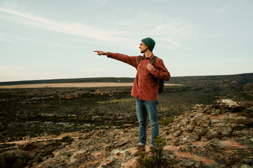 Caucasian male free spirit hiking in mountain pointing in distance looking over horizon