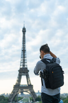 Back view of tourist with backpack taking picture of Eiffel tower.
