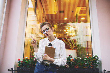 smart woman with short hair holds notepad in hand and glasses on face exterior window