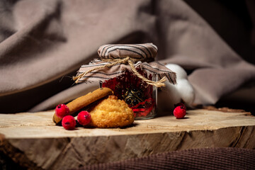 A jar and cookies with berries lie on a wooden board on a brown background