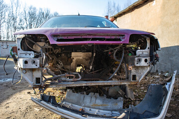 An old, disassembled, rusty car with no engine or wheels rusts in a scrapped area.