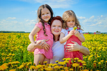 Mother and two daughters in a field with yellow dandelions. family walks in the spring in nature