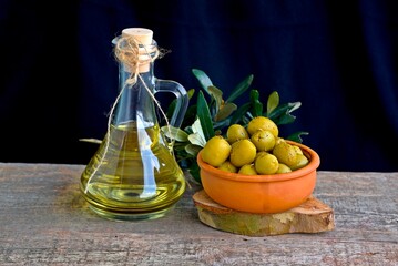 Olive branch with olive oil in a glass bottle and green olives on a plate on a wooden background