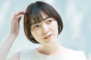 Fototapeta premium 髪を整える女性と、白壁に映る木々の影