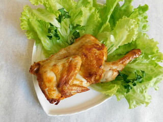 half of the grilled chicken and lettuce leaves are on a white plate.