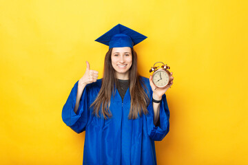 Photo of happy woman graduating showing thumb up and alarm clock over yellow background