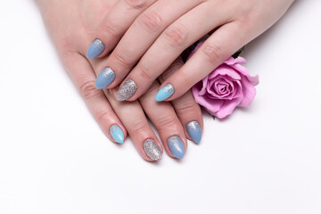Obraz na płótnie Canvas blue manicure on sharp long nails with silver sparkles on a white background with a pink rose in hands