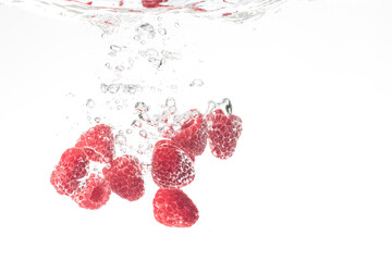 Raspberries splashing in water on white