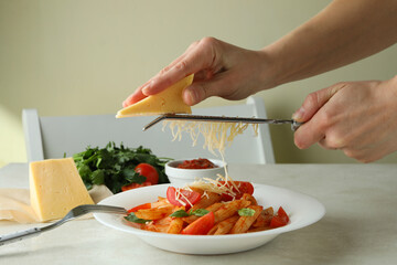 Woman rubs cheese on pasta with tomato sauce