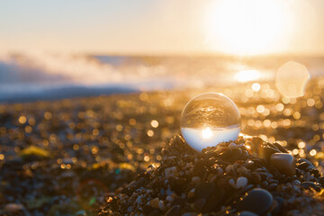 Glass round ball on the beach reflects the sea in summer at sunset
