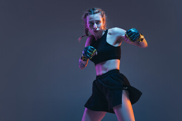 Young female MMA fighter training isolated over blue background in neon light