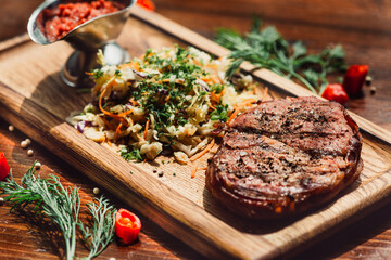 Grilled beefsteaks with salad and red sauce on wooden board. Close up.